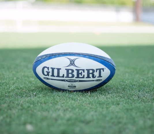 Wales squad named for Wheelchair Rugby League World Cup A photo of a Rugby ball with the text "GILBERT" on it underlined. It is in the middle of a rugby pitch.